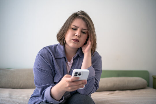 Serious plus size woman checking smartphone on sofa, online notification, mobile communication, screen addiction, home lifestyle, digital worry.