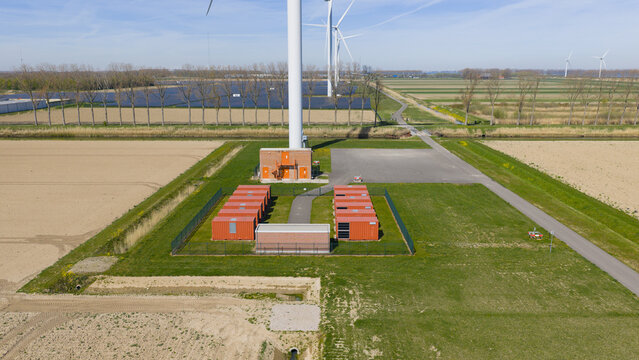 Aerial view of a wind turbine base with orange storage containers and a solar farm in the background Middelharnis, Zuid-Holland, Netherlands.