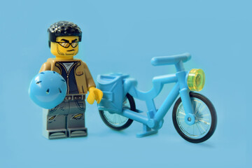 Naklejka premium Lego minifigure of biker with hardhat and bicycle or bike isolated on blue. Editorial illustrative image of popular plastic toy constructor for children.