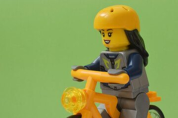 Naklejka premium Lego minifigure of biker in yellow hardhat and bicycle or bike isolated on green. Editorial illustrative image of popular plastic toy constructor for children.