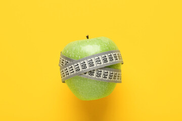 Naklejka premium Fresh apple with white measuring tape on yellow background. Diet concept