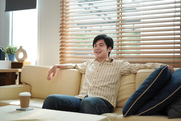 Obraz premium Young man relaxing on couch, Relaxed man sitting on comfortable sofa with coffee cup on table enjoying good quiet peaceful time alone at home