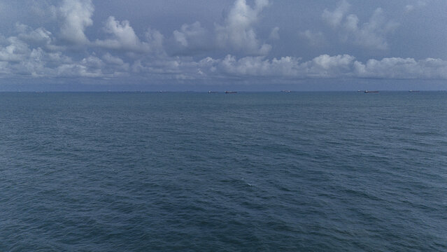 Aerial view of the vast blue ocean with cargo ships on the horizon under a cloudy sky in Badagry, Lagos, Nigeria.