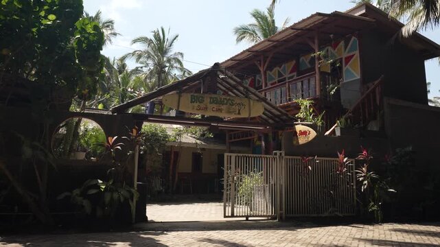 Entrance of rustic surf camp with tropical plants and wooden features in sunlight