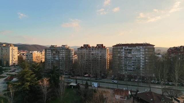 Drone aerial flying over a residential city district in Nis Serbia with high rise apartment buildings an open air market and a setting sun illuminating the cityscape in warm golden light