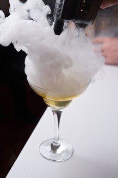Bartender Using Smoke Gun to Infuse Cocktail. Close-up of a bartender using a professional smoking gun to create a thick vapor cloud over a golden cocktail in a coupe glass