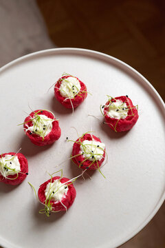 Close-up of elegant red choux pastry appetizers filled with white mousse, garnished with sprouts and sesame on a white plate. Gourmet catering, buffet, banquet, or wedding reception scene