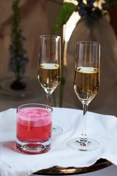 Close-up of two champagne flutes and a pink cocktail with foam on a white tablecloth. Elegant drinks for a luxury celebration, wedding reception, or banquet event