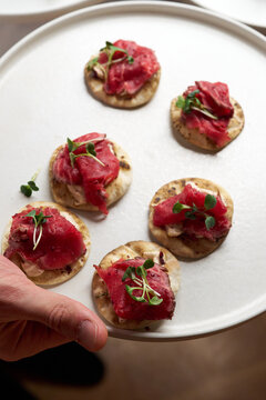 Close-up of a hand holding a white plate with roast beef crostini appetizers garnish with microgreens. Elegant gourmet catering for a banquet, wedding reception, or corporate event