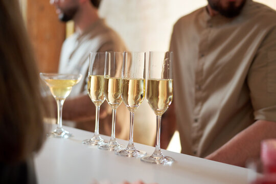 Close-up of four champagne flutes and a martini glass filled with sparkling wine on a white bar counter. Elegant drinks served during a luxury event, banquet, or wedding reception