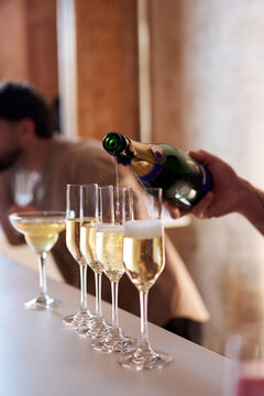 Close-up of a waiter pouring sparkling champagne from a bottle into elegant flutes on a bar counter. Luxury celebration, wedding reception, or banquet event