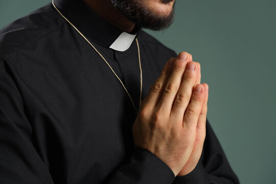 Young priest praying on green background, closeup