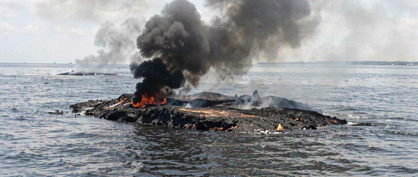A black smoke rises from a rock submerged in water, a dramatic and intense scene
