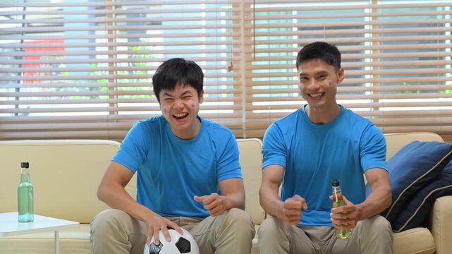 Friends watching soccer game at home, Two men react to match on sofa.