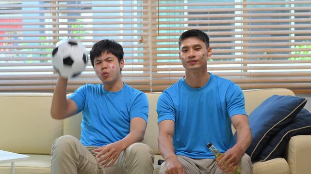 Friends watching soccer game at home, Two men react to match on sofa.
