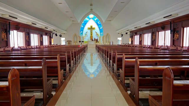 Interior of Saint Francis Xavier Church in Kuta, Bali, featuring long wooden pews, high vaulted ceiling, bright altar cross, and peaceful sacred atmosphere.