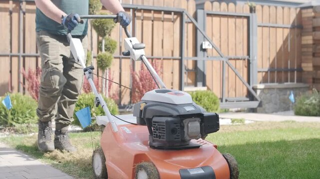 A man uses a professional gasoline scarifier to remove moss and thatch from a green lawn in a private house backyard.