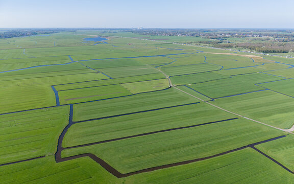 Aerial view of vast green polder fields with a network of drainage canals under a clear blue sky Heiloo, North Holland, Netherlands.