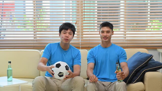 Friends watching soccer game at home, Two men react to match on sofa.