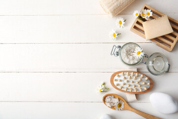 Fototapeta na wymiar Composition with spa stones, massage body brush, chamomile flowers and glass jar of sea salt on white wooden background, closeup