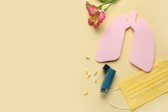 Asthma inhaler with paper lungs, medical mask and flower on beige background