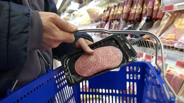 Close-up of a customer's hands putting a package of sliced salami into a shopping cart