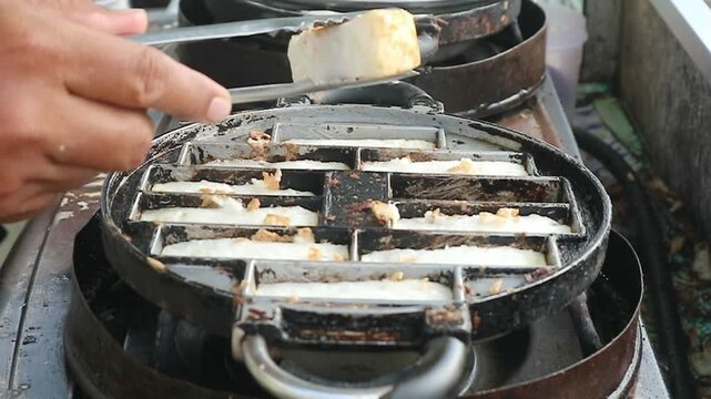 The process of lifting the cooked pancong cake from the pan using a knife and tongs to make it easy to remove from the pan.