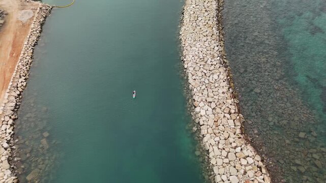 Aerial view of rocky breakwater and calm sea with lone paddleboarder
