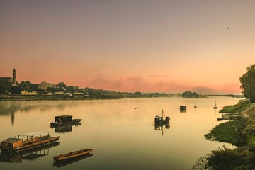 Fototapeta premium Golden hues reflect off the calm waters of the Loire River as boats gently bob in the soft evening light. Blois lies peacefully in the backdrop, blending history with stunning landscapes