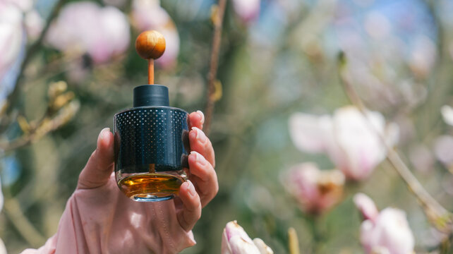 Hand holding a dark glass perfume bottle with amber liquid and wooden stopper