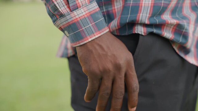 Gentle father in relaxed field stance. Male figure in casual attire observing calmly outdoors. Father with his hand in pocket in tranquil grassy environment appears thoughtful and protective