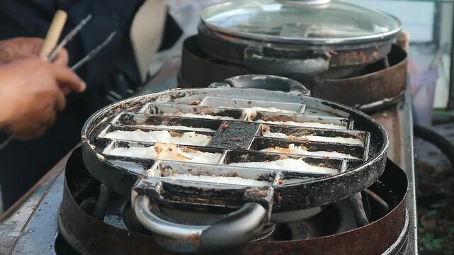 The process of lifting the cooked pancong cake from the pan using a knife and tongs to make it easy to remove from the pan.