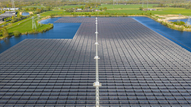 Aerial view of the Sekdoornse Plas floating solar farm featuring thousands of photovoltaic panels on a lake surrounded by green fields and power lines in Zwolle, Overijssel, Netherlands.