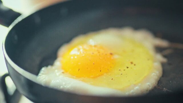 A chef gently cracks an egg into a hot frying pan, the sizzle echoing in a bright kitchen. The cook watches the yolk set, mastering the simple yet essential technique of pan-frying for breakfast