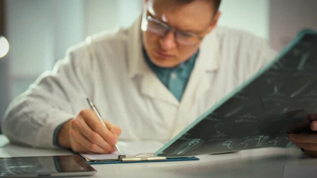 A doctor carefully fills out a medical record while examining an MRI printout of the injury, viewing multiple projections to plan an integrated fracture treatment in a bright office