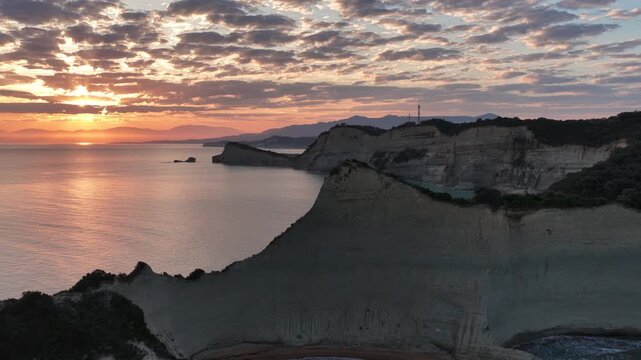 Aerial panning shot of majestic white cliffs at Cape Drastis during golden sunrise over the Ionian Sea, stunning coastal landscape of Corfu Island Greece, nature travel scenery
