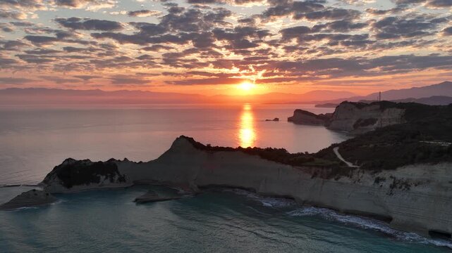 Majestic sunrise over the unique rock formations of Cape Drastis, Corfu, Greece. Aerial drone shot capturing the dramatic coastline and golden sun reflection on the tranquil Ionian Sea
