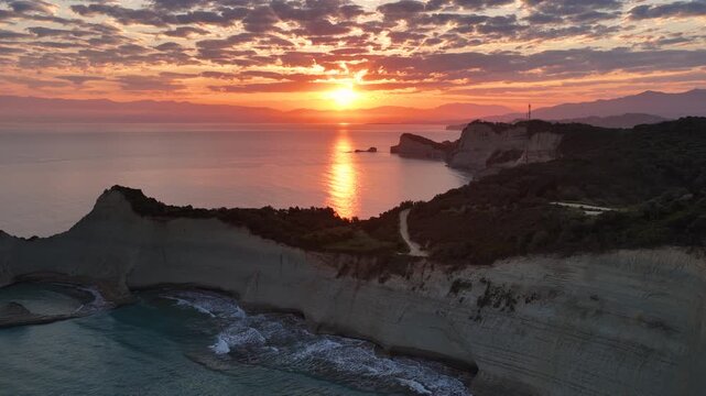 Stunning drone video of Cape Drastis white cliffs at sunrise, Corfu island, Greece. Golden hour sunlight reflecting on the calm Ionian Sea. Breathtaking European coastal landscape