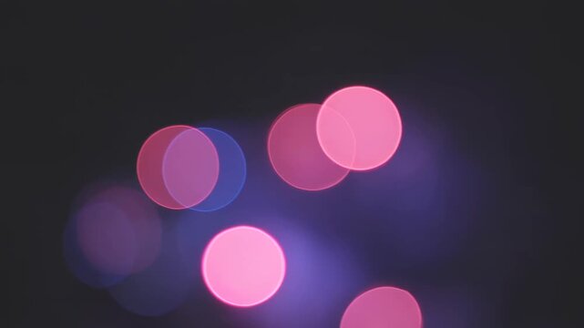 Soft luminous circles of pink and blue light gently shimmer and drift through the dark, creating an abstract bokeh glow at night