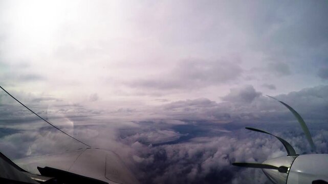 Cinematic point-of-view shot from inside an airplane cockpit flying above a dense layer of clouds under a dramatic sky. The footage captures the wing and propeller in motion, offering an immersive avi