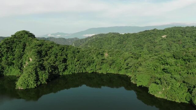 Aerial slow flyover of lush green forest bordering calm reflective lake surface