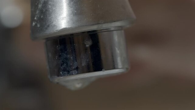 Close up of an old dirty calcified bathroom faucet dripping some water