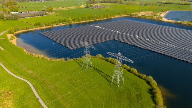 Aerial view of the floating solar farm on Sekdoornse Plas with high-voltage power lines and green fields in Zwolle, Overijssel, Netherlands.