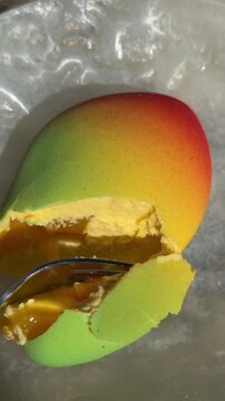 Vertical screen mango shaped dessert broken with fork revealing soft creamy filling inside close up sweet food moment with satisfying texture