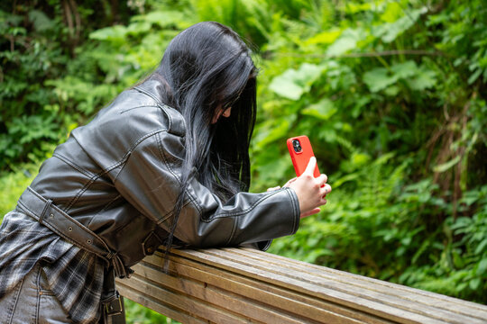 Young Woman Taking Photo with Red Smartphone in Green Forest, Outdoor Lifestyle and Social Media Concept