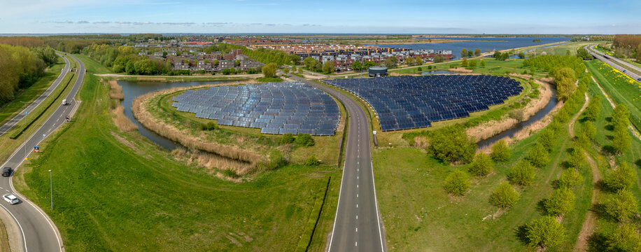 Aerial view of a bus road running through the solar energy installation at Zonneiland Almere with photovoltaic panels set within a green and water-rich landscape.