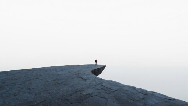 Lone Person Standing on Edge of High Cliff Above Clouds in Minimalist Foggy Landscape