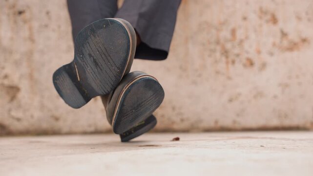 Closeup caucasian man shoes tapping over concrete ledge legs swinging worn soles textured leather urban stillness subtle rhythm casual trousers neutral wall background motion loop