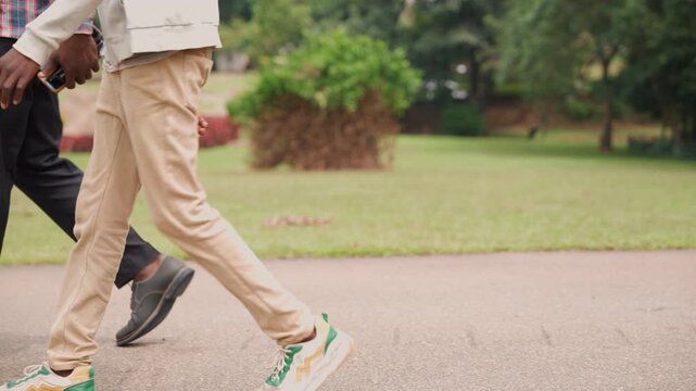 Closeup of father and son walking side by side. Synchronized steps of father and son along paved trail. Casual stroll capturing their coordinated movement and steady rhythm on path