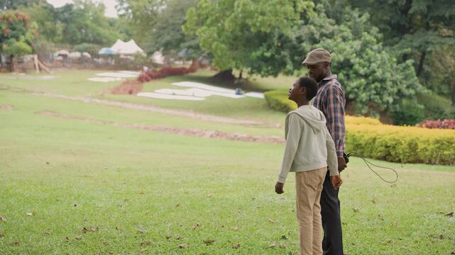 Father and son observe. Parent and child gaze skyward casually. Father guides son as they look at nature together. Tranquil moment shared between father and son observing sky and lush greenery